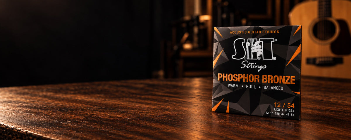 S.I.T. Phosphor Bronze Acoustic Guitar Strings P1254 Light in the new packaging, on a wood table with an acoustic guitar behind it